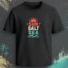 Black regular-fit T-shirt with “Sun Salt Sea” coral, cream, and aqua beach graphic featuring sun and wave artwork.